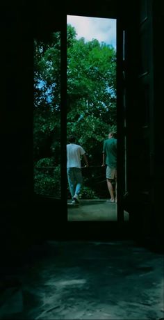 two people walking through an open door in the dark, with trees behind them and one person holding onto another persons hand