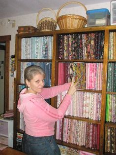 a woman standing in front of a book shelf filled with fabrics