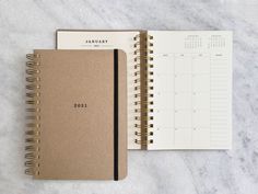 a spiral notebook with the letter m on it next to an open planner and pen