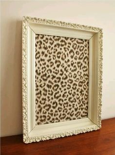 a white frame sitting on top of a wooden table next to a wall with a leopard print