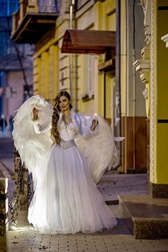 a woman dressed in an angel costume is standing on the street with her arms outstretched