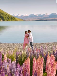 two people standing next to each other on a beach with flowers in the foreground