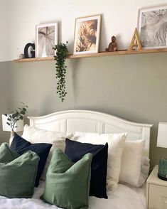 a white bed topped with lots of pillows next to a shelf filled with pictures and plants