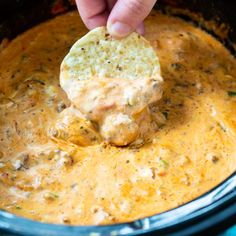 a hand dipping a tortilla chip into a slow cooker filled with cheese