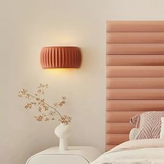 a bedroom with a pink headboard and white bed in the foreground is a vase with flowers on it