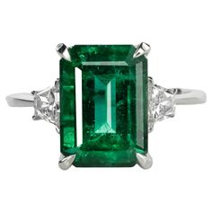 Presenting a truly remarkable piece, this ring holds a captivating allure with its centerpiece—a dazzling 13 carat shape emerald Zambian emerald, certified by the AGL Embraced by two trapezoid white-shaped diamonds weighing a total of 1 carat, this ring exudes opulence and sophistication. The emerald, of exceptional gem quality, boasts a vivid green color that captures the essence of nature's beauty, enhanced by its fine lustre and brilliant sparkle. This ring is more than a piece of jewelry; it's an embodiment of elegance, style, and the timeless allure of a emerald shaped gem. Make a statement with this extraordinary ring, a symbol of love and refined taste. Emerald Statement Ring, Colombian Emerald Ring, Verdant Green, Emerald Wedding Rings, Contemporary Engagement Rings, Platinum Diamond Rings, Emerald Diamond Ring, Bracelet Love, Zambian Emerald