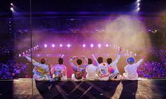 group of people sitting on stage with their arms in the air and fireworks coming from behind them