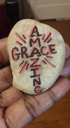 a hand holding a rock with the word grace written on it in black and red