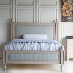 a white bed sitting in a bedroom next to a painting on the side of a wall