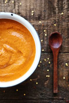 a white bowl filled with carrot soup next to a wooden spoon on top of a table