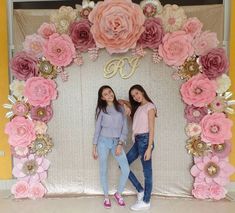 two girls standing in front of a backdrop with flowers