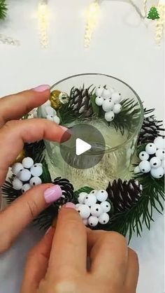 two hands are decorating a glass with pine cones and white berries on the rim