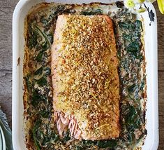 baked salmon with spinach and garlic in a white dish on a wooden table next to silverware