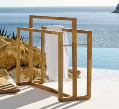 a towel rack sitting on top of a wooden deck next to the ocean with towels hanging from it