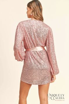 Light up the room with your magnificent self in the Samantha Pink Sequined Long Sleeve Wrap Dress! Sparkly pink sequins (atop gauzy beige woven fabric) dazzle across a wrapping bodice (that secures with a hidden snap and two internal ties) and long sleeves with gathered shoulders and elastic cuffs. Matching satin sash belt cinches the waist above a wrap mini skirt. - Lined - Dress: 50% PET, and 50% Polyester - Lining: 100% Polyester - Fits True To Size (S: 2-4, M: 6-8, L:10-12) - Hand Wash Cold. Pink Embellished Sequin Fabric For Cocktail, Spring V-neck Glamorous Sequin Fabric, Pink Contrast Sequin Mini Dress For Holidays, Holiday Mini Dress With Contrast Sequin In Pink, Spring Dress With Sequins And Surplice Neckline, Sequin Surplice Neckline Dress For Party Season, Sequin Dress With Surplice Neckline For Date Night, Sequin Surplice Neckline Dress For Date Night, Pink Embellished V-neck Sequin Dress