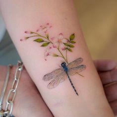 a woman's arm with a dragonfly and flowers tattoo on the left forearm