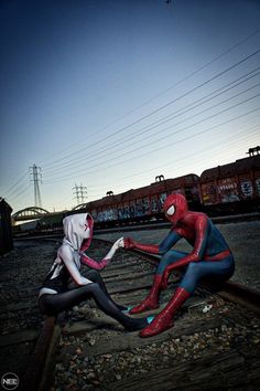 two spider - man cosplayes are sitting on train tracks