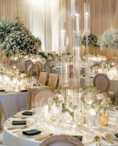 the tables are set up for an elegant wedding reception with tall centerpieces and flowers