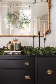 a black dresser with candles and evergreen garland on top