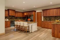 a large kitchen with wooden cabinets and marble counter tops is pictured in this image, there are four bar stools at the center of the island