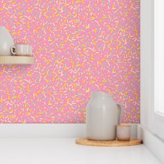 a pink wall with sprinkles on it and two white vases in the foreground