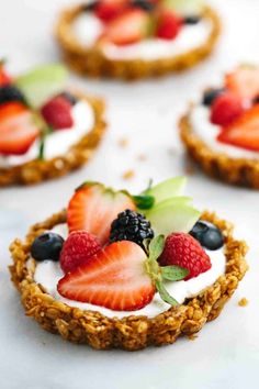 small desserts with strawberries, blueberries and kiwi on top are arranged on a white surface