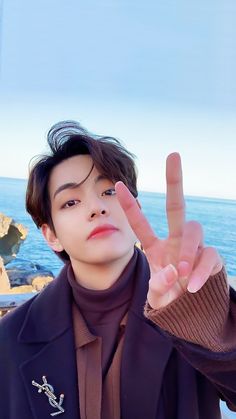 a young man making the v sign with his hand while standing next to the ocean