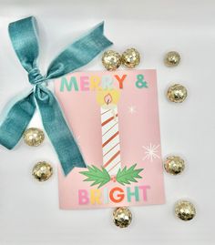 a pink card with a blue ribbon and some gold candies around it on a white surface