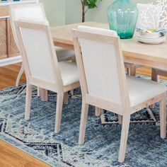 a dining room table with white chairs and blue rug