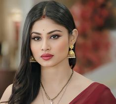 a woman with long black hair wearing gold earrings and a red dress is looking at the camera