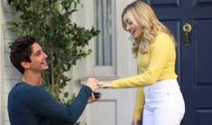 a man is handing something to a woman in front of a house with blue doors