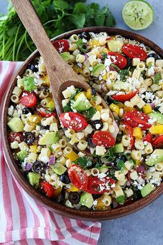 a bowl filled with pasta salad next to a wooden spoon on top of a striped towel