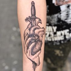 a black and white tattoo on the arm of a person with a knife in his heart