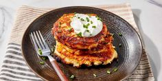 two pancakes with sour cream and chives on a black plate next to a fork