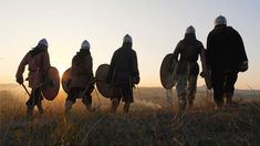 three men in medieval costumes are walking through the grass with shields and shieldes on their backs