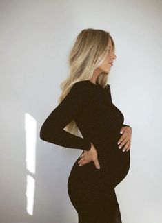 a pregnant woman in a black dress poses for the camera with her hands on her hips