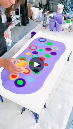 a woman is making an art project with colored circles on the paper and plastic cups in front of her