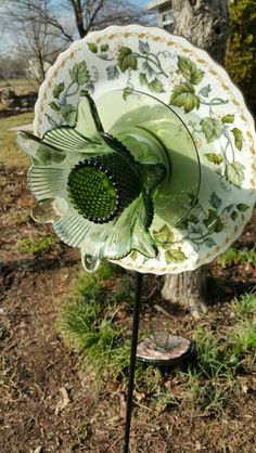 a green and white flower sitting on top of a metal pole next to a tree