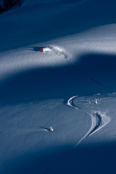 a man riding skis down a snow covered slope next to a red object in the distance