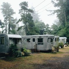 an old trailer sits in the middle of a field with trees and bushes around it