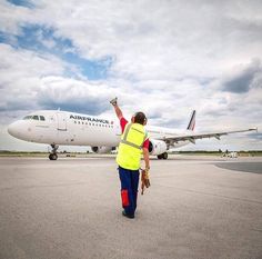 a man in yellow vest walking towards an airplane on tarmac with it's landing gear down