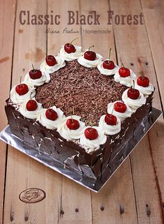 a chocolate cake with cherries and whipped cream on top sits on a wooden table