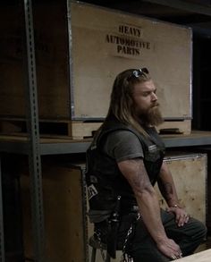 a man with long hair and beard sitting on a stool in front of some boxes