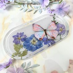 two butterflies sitting on top of purple flowers in a glass container with blue and white flowers around it