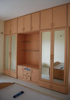 an empty room with wooden cupboards and mirrors on the wall, in front of a bed