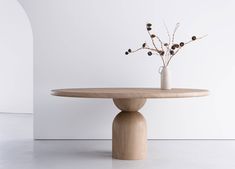 a vase with some flowers sitting on top of a wooden table in front of a white wall