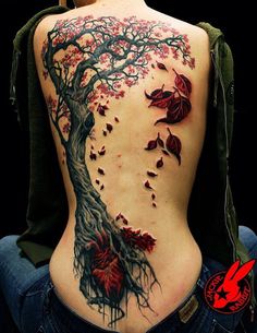 the back of a woman's body with red flowers and tree tattoo on it