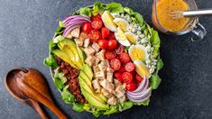 a salad with chicken, lettuce, tomatoes, onions and avocado next to a glass of orange juice