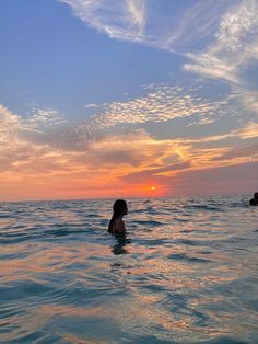 two people in the ocean at sunset with one person swimming towards the camera and the other sitting on his back