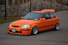 an orange car parked in front of a stone wall